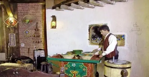 مردی با لباس سنتی در حال آماده سازی غذاهای ایرانی در رستوران ترمه، فضایی دلنشین با دکوراسیون اصیل و بومی.