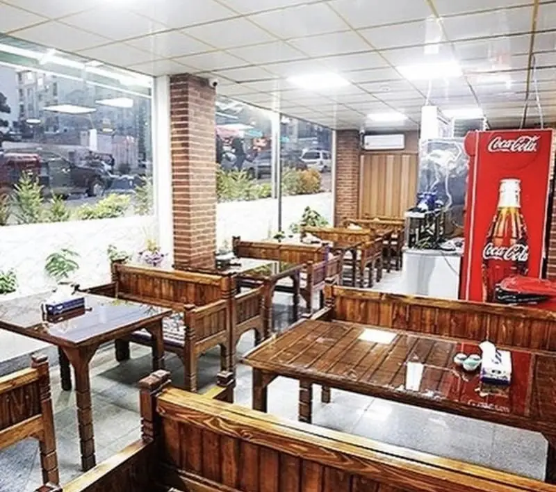 فضای داخلی زیبای کبابی سرزمین جگر با میزهای چوبی، نیمکت‌های راحت، ستون آجری و پنجره‌ای بزرگ رو به خیابان. محیطی دلنشین برای صرف جگر.