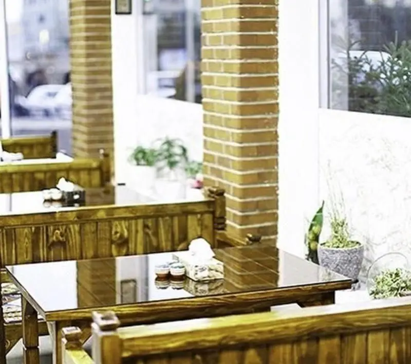 محیط داخلی دنج و دلنشین کبابی سرزمین جگر با دکوراسیون چوبی، میزهای شیشه‌ای و فضای غذاخوری سنتی و جذاب.