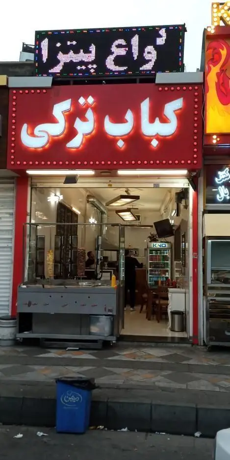 نمایی از فست فود وینر برگر با تابلوهای کباب ترکی و انواع پیتزا. ورودی مغازه با دستگاه‌های دونر و فضای داخلی میز و صندلی.