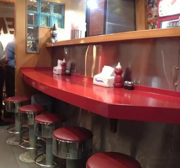 پیشخوان قرمز و صندلی های استیل پیتزا سورن. فضای دنج و دلنشین فست فود سورن برای تجربه ای لذت بخش از پیتزا و غذای محبوب.