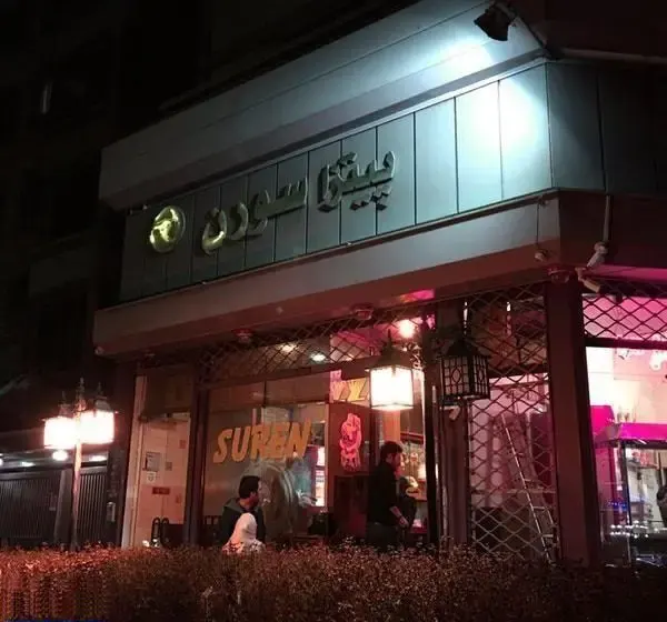 نمای بیرونی رستوران پیتزا سورن در شب با تابلوی روشن پیتزا سورن و نام انگلیسی SUREN، مکانی دنج با مشتریان داخل برای صرف انواع فست فود و پیتزاهای خوشمزه.