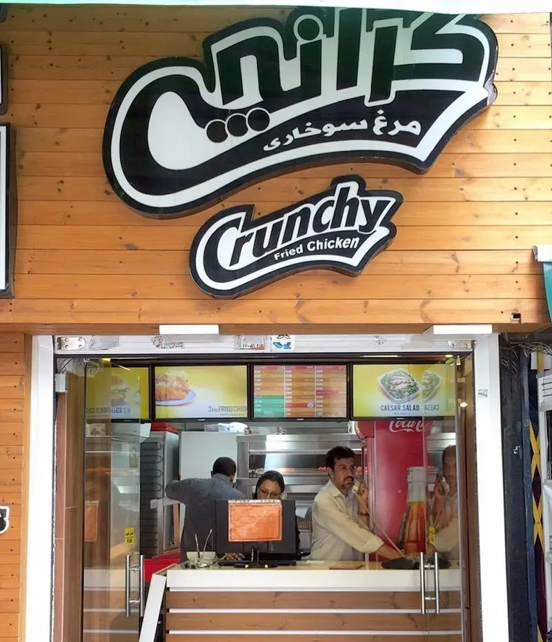 تصویر رستوران فست فود کرانچی: نمای بیرونی جذاب با تابلوی "مرغ سوخاری" و محیط داخلی فعال و پرسنل.