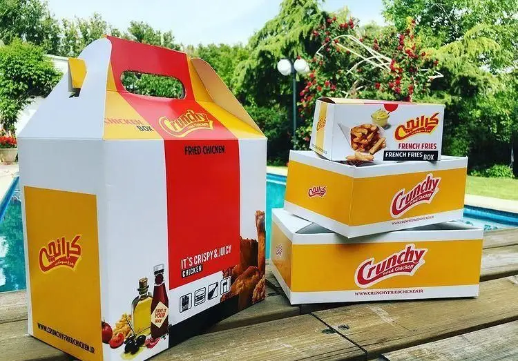 بسته بندی محصولات فست فود کرانچی شامل جعبه بزرگ مرغ سوخاری و باکس‌های سیب زمینی با لوگو جذاب کرانچی.