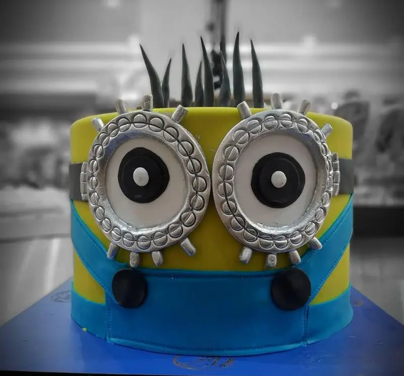 کیک مینیون زرد و آبی با چشمان بزرگ نقره‌ای و موهای مشکی، یک شاهکار از قنادی اصل تبریز برای جشن تولد و کودکان.