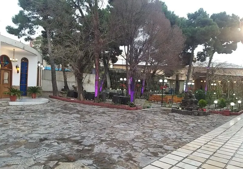 نمایی از محوطه باغ رستوران نارون با فضای باز سرسبز، میز و صندلی‌های چوبی، نورپردازی بنفش و حوضچه سنگی دلنشین برای مشتریان.