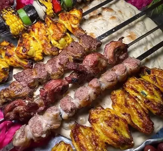 انواع کباب شامل جگر، گوشت، جوجه، بال، بلال ذرت تازه و سبزیجات روی نان داغ در جگرکی بابا شمل. تجربه‌ای لذیذ از غذای ایرانی.
