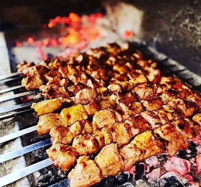تصویر کباب‌های گوشت تازه و آبدار در حال گریل شدن روی ذغال داغ در "جگرکی بابا شمل"، تجربه‌ای لذیذ از کباب سنتی.
