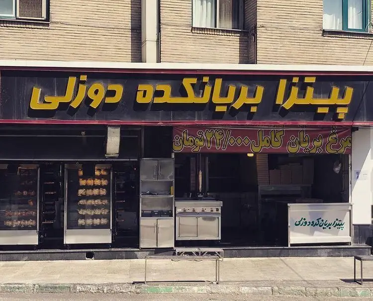 نمای بیرونی پیتزا بریانکده دوزلی، یک رستوران فست فود با تابلو مشخص، دستگاه‌های مرغ بریان و ارائه پیتزا.