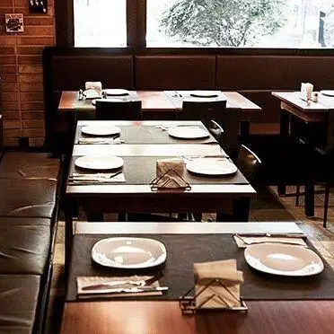 نمایی از فضای داخلی رستوران تکسین با میزهای چیدمان شده، صندلی‌های چرمی قهوه‌ای و پنجره‌های بزرگ، محیطی دنج و شیک برای مشتریان.