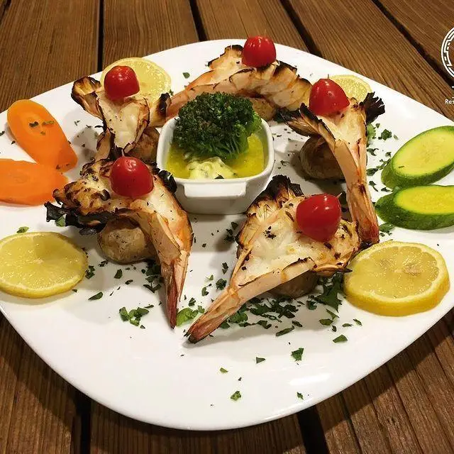 بشقاب شیک میگوهای گریل‌شده آبدار با گوجه‌فرنگی گیلاسی، لیموی تازه، کلم بروکلی و سس. شاهکار غذای دریایی رستوران تکسین.