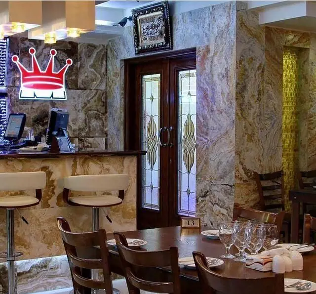 فضای داخلی مجلل رستوران ایرانی در شهرری، شامل میزهای غذاخوری آماده و بار شیک با دیوارپوش سنگ طبیعی، مناسب تجربه ای خاص.