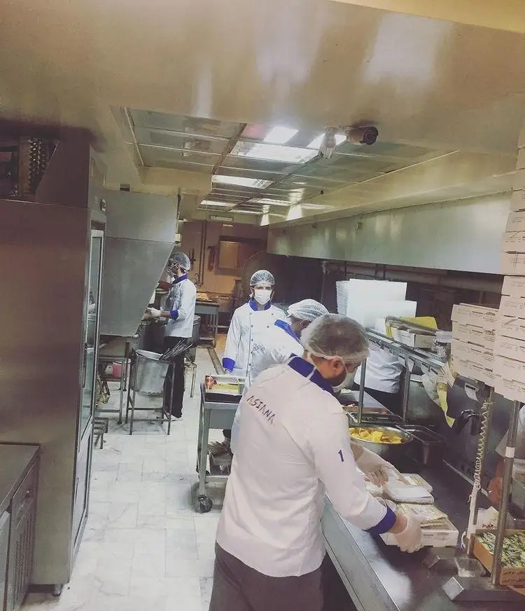 تصویری از کارکنان آشپزخانه آسیانا که با رعایت کامل پروتکلهای بهداشتی در حال آمادهسازی و بستهبندی غذا هستند.
