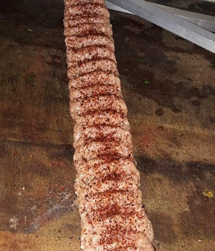 کباب آدانا یا اورفا خام و چاشنی‌زده شده روی تخته قصابی، آماده طبخ توسط سرآشپزهای ماهر در رستوران نارنج برای تجربه طعمی بی‌نظیر.