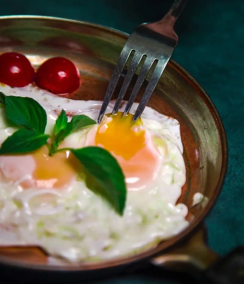 یک صبحانه عالی و دلچسب از کافه رستوران عمو سهراب. نیمروهای تازه و خوشرنگ در تابه مسی با گوجه گیلاسی و برگ‌های سبز معطر، آماده برای سرو.