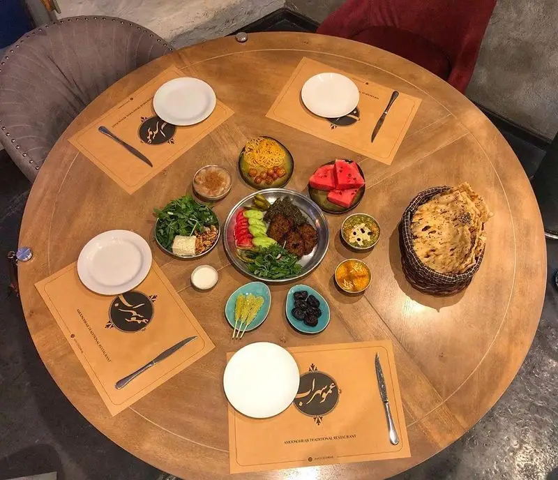میز گرد پر از غذای سنتی و کباب ایرانی در کافه رستوران عمو سهراب، با نان تازه و سبزیجات متنوع برای تجربه‌ای لذت‌بخش.