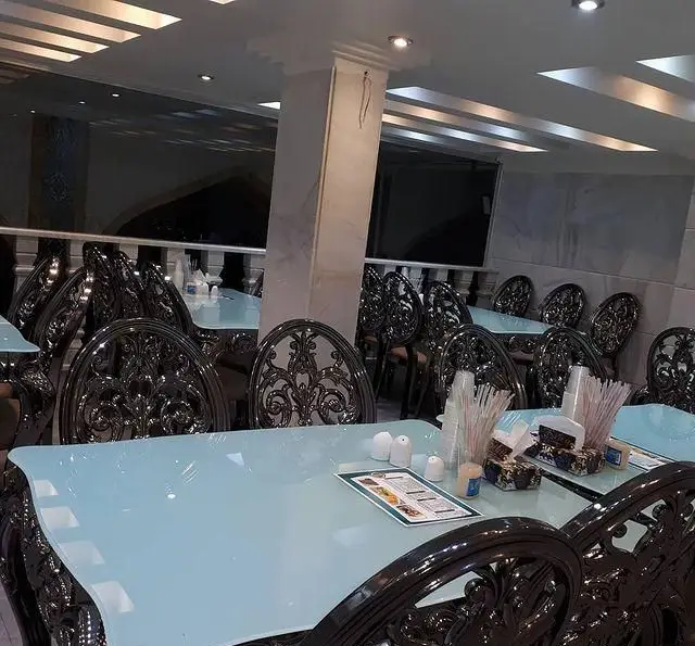 فضای داخلی شیک کبابسرای الغدیر با میزهای شیشه‌ای آبی و صندلی‌های چوبی منبت‌کاری شده برای تجربه‌ای دلنشین از غذاخوری.