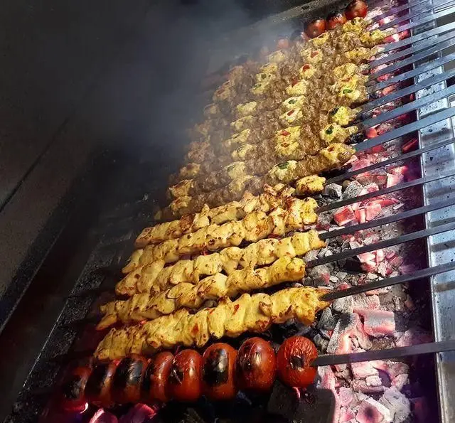 کباب کوبیده و جوجه کباب ذغالی در حال پخت بر روی آتش داغ، همراه با گوجه‌های کبابی تازه در کبابسرای الغدیر.