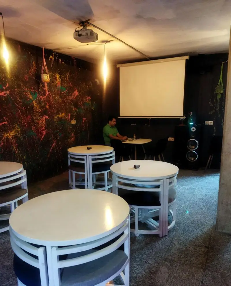 فضای داخلی مدرن و جذاب لیون کافه با دیوارنگاره رنگارنگ هنری، میز و صندلی‌های شیک، پروژکتور و اسپیکرهای قدرتمند برای رویدادها و دورهمی‌ها.