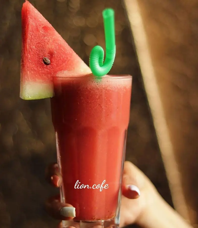 یک لیوان اسموتی یا آب هندوانه تازه و خنک لیون کافه با تزیین برش میوه هندوانه و نی سبز خمیده. نوشیدنی جذاب و خوشرنگ تابستانی.