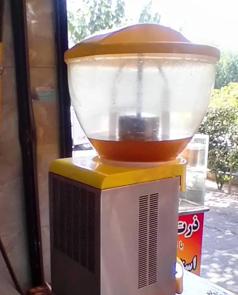 دستگاه مخصوص آبمیوه و شربت پرتقال در مغازه آبمیوه بستنی دلتا، تضمین کننده تازگی و کیفیت نوشیدنی‌های خنک.