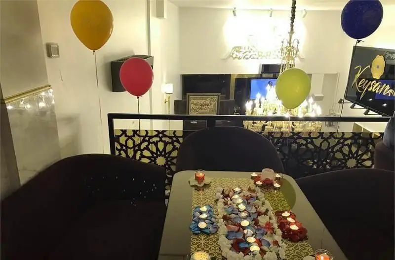 تصویری از کافی شاپ کیسان با دکوراسیون شیک و رمانتیک برای جشن، شامل میز آرایی با گلبرگ، شمع و بادکنک‌های رنگی. محیطی ایده‌آل برای مناسبت‌های خاص.
