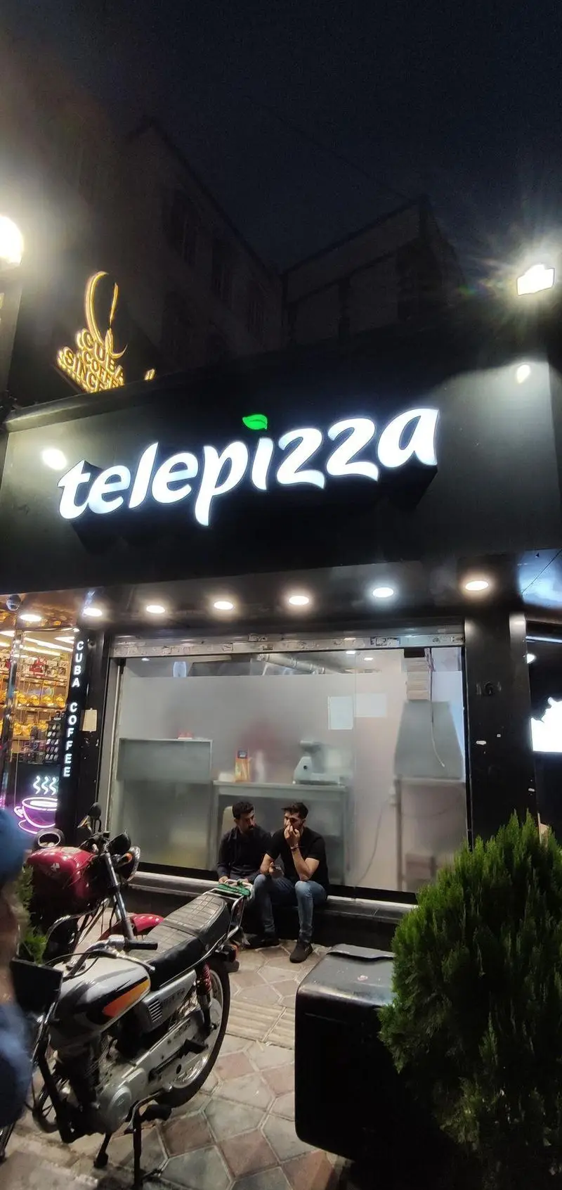 تله پیتزا شعبه پاسداران تهران در شب. تابلوی روشن و جذاب فست فود Telepizza با لوگوی برگ سبز و تابلوی Cuba Coffee در کنار آن.