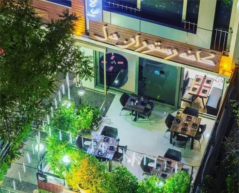 تصویری هوایی از کافه فرانسوی ویوات در شب، شامل فضای بیرونی با میز و صندلی‌های چوبی، گلدان‌ها و نورپردازی جذاب.