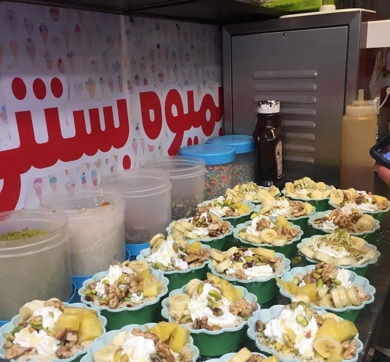 ویترین مملو از دسرهای خوشمزه آبمیوه فردین، شامل بستنی‌های میوه‌ای، موز، آناناس، پسته، گردو و سس‌های متنوع آماده فروش.