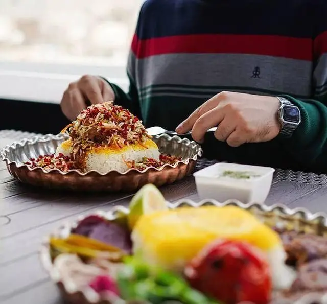مشتری در رستوران شالِت در حال صرف غذای ایرانی شامل برنج زعفرانی با زرشک و خلال بادام، در محیطی دلنشین و با کیفیت.