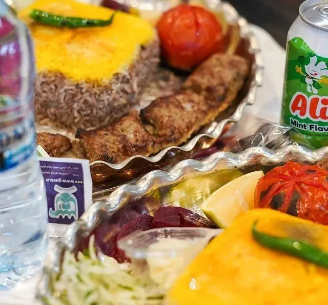 نمایی نزدیک از سینی غذای رستوران شالِت شامل چلوکباب کوبیده، برنج زعفرانی، گوجه، لیمو و نوشیدنی علی با طعم نعنا، یک غذای سنتی و خوشمزه ایرانی.