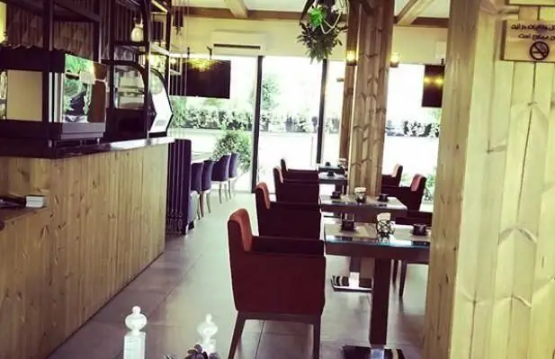 محیط داخلی دلنشین و زیبای کافی شاپ سبو با پیشخوان چوبی شیک، دستگاه قهوه‌ساز، میز و صندلی‌های راحت و پنجره‌های بزرگ با چشم‌انداز فضای سبز.