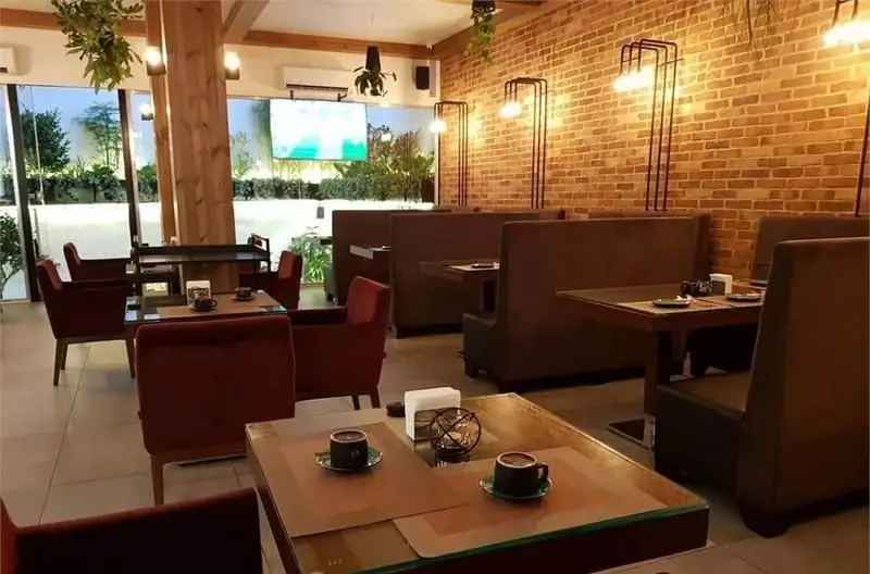 نمایی از محیط داخلی گرم و دعوت‌کننده کافی شاپ سبو با چیدمان متنوع میز و صندلی، دیوارهای آجری جذاب و پنجره‌های بزرگ رو به بیرون.