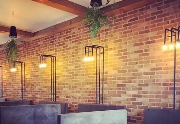 دکوراسیون داخلی مدرن و جذاب کافی شاپ سبو با دیوار آجری، نورپردازی صنعتی شیک و مبلمان راحتی. فضایی دنج و دلنشین برای مشتریان.