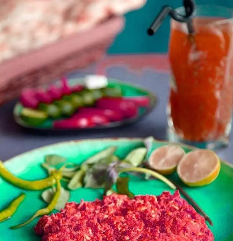 میز رنگارنگ کافه سبو: بشقاب مزه با غذای قرمز رنگ، فلفل سبز، لیمو، ترشیجات متنوع و نوشیدنی خنک، آماده پذیرایی از مشتریان.