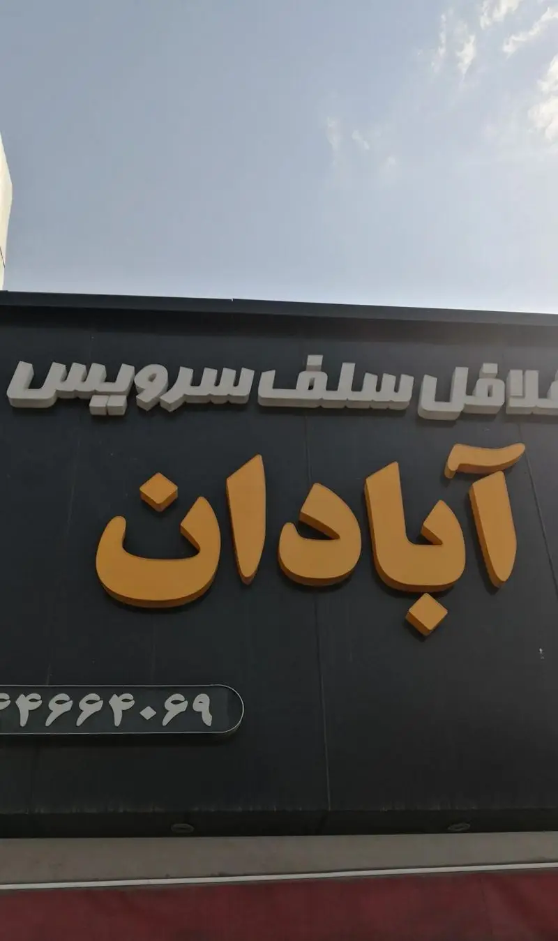 تابلو بزرگ فلافل سلف سرویس آبادان، ارائه دهنده فلافل‌های خوشمزه و غذای سلف سرویس، با حروف برجسته طلایی و سفید، شامل شماره تماس برای سهولت سفارش غذا.