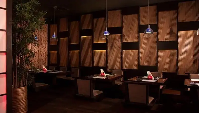 نمایی زیبا از فضای داخلی رستوران کنزو با دکوراسیون شیک و مدرن ژاپنی، میز و صندلی های چوبی تیره، پنل های دیواری موج دار و نورپردازی چشم‌نواز.