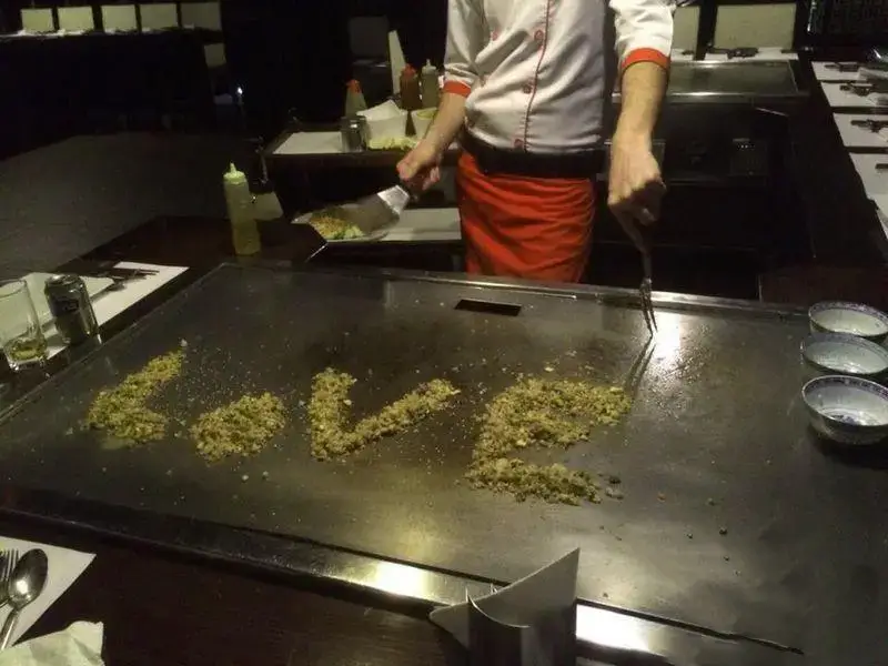 سرآشپز رستوران کنزو در حال آشپزی هنرمندانه روی گریل تپانیاکی و ساخت کلمه LOVE با مواد غذایی برای تجربه ای رمانتیک.