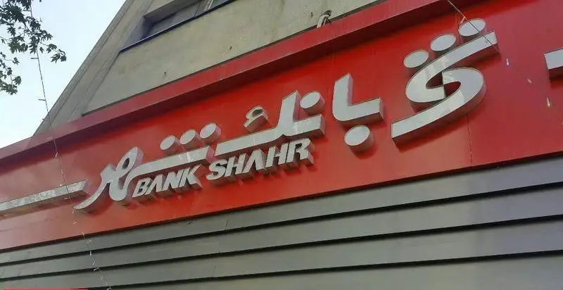 نمای نزدیک از تابلوی شعبه بانک شهر کاووسیه با حروف برجسته سفید بر زمینه قرمز، شامل نام فارسی و انگلیسی Bank Shahr.