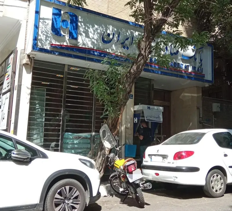 نمای واضح از شعبه بانک صادرات احتشامیه، با تابلوی مشخص، دستگاه خودپرداز در دسترس و فضای پارکینگ با چند خودرو.