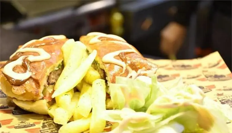 ساندویچ برگر ویژه گاراژ برگر با سس‌های لذیذ، همراه سیب زمینی سرخ کرده و کاهو تازه، یک غذای فست فود خوشمزه.