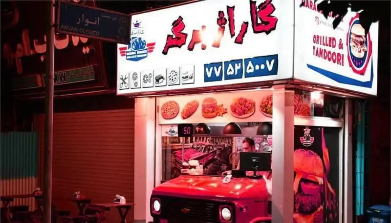 فست فود گاراژ برگر در شب، با پیشخوان شبیه خودروی قرمز، عرضه کننده انواع همبرگر، پیتزا، ساندویچ، کباب و غذای تنوری، آماده سفارش.
