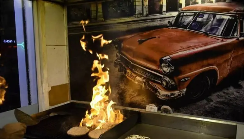 برگرهای آبدار گاراژ برگر بر روی گریل شعله‌ور، در فضایی با تصویر ماشین کلاسیک. تجربه‌ای بی‌نظیر از غذای آماده و طعمی فراموش نشدنی.