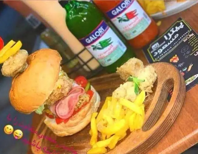 ساندویچ مرغ و ژامبون لذیذ با سیب‌زمینی سرخ‌شده و سس‌های گالوری، سرو شده روی تخته چوبی، همراه با منوی پیتزا مسعود.