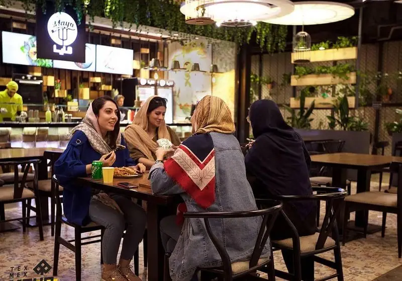 محیط دلنشین رستوران مايا تِكس مِكس؛ چهار خانم جوان در حال لذت بردن از غذای لذیذ و دورهمی دوستانه در فضایی با دکوراسیون گیاهی.