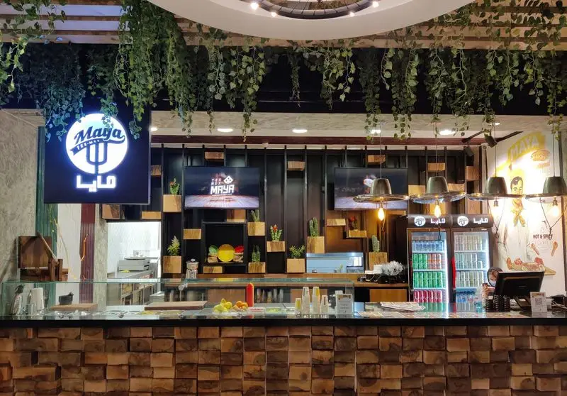 دکوراسیون داخلی مدرن رستوران مايا تِكس مِكس: کانتر چوبی با جزئیات بلوکی، گیاهان سبز آویزان و نورپردازی جذاب. فضایی خاص برای غذای مکزیکی.