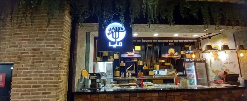 ورودی و پیشخوان رستوران مايا تِكس مِكس در شب، با تابلوی نئونی 'Maya Tex-Mex' و فضای گرم و آماده برای میزبانی.