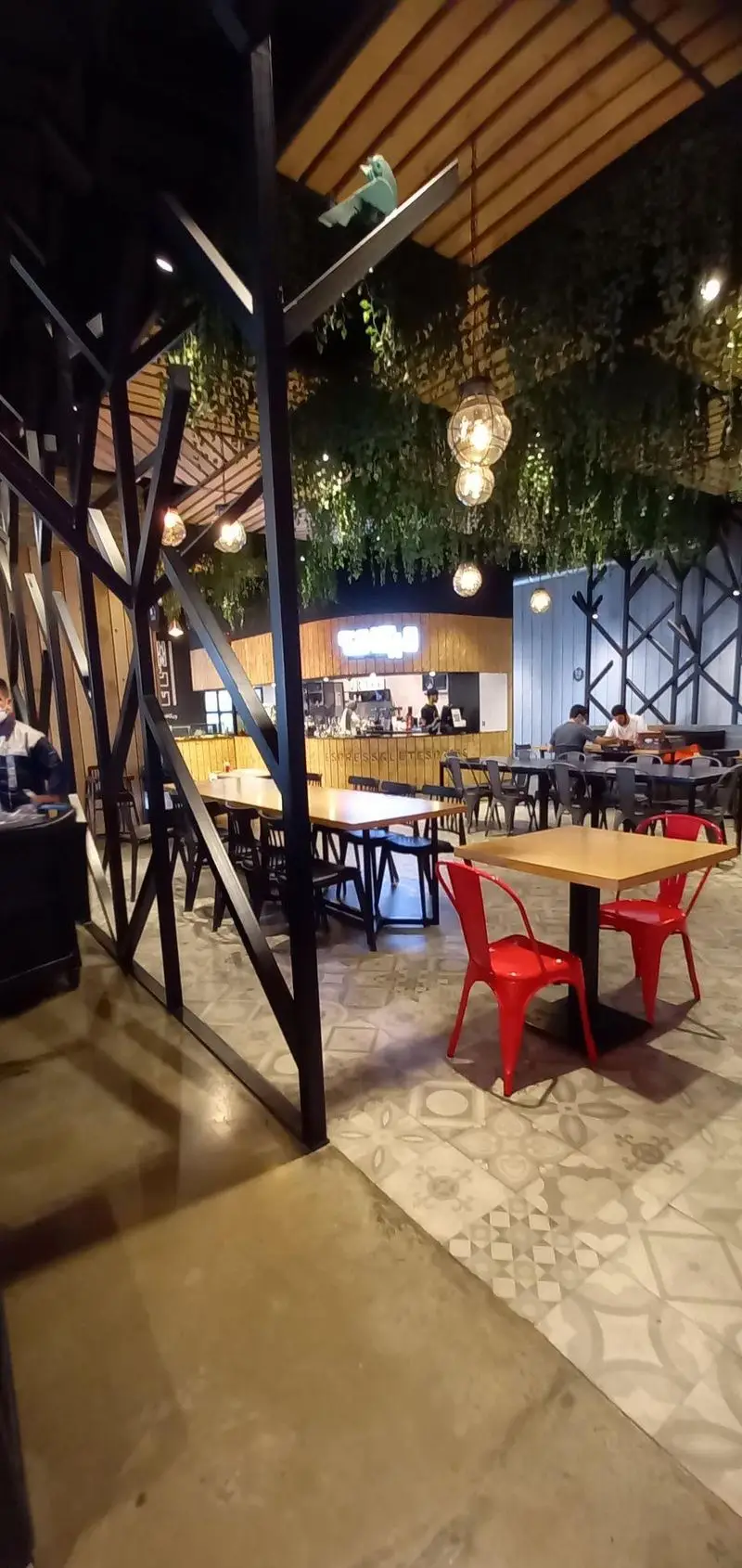 نمایی از دکوراسیون داخلی شیک و مدرن رستوران مايا تِكس مِكس با میزهای چوبی، صندلی‌های قرمز، سقف گیاهی، نورپردازی گرم و محیطی دوستانه.