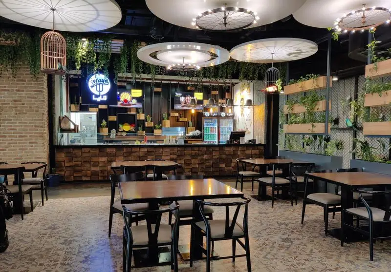 فضای داخلی رستوران مايا تِكس مِكس با طراحی مدرن، میزهای غذاخوری چوبی، گیاهان سبز آویز و نورپردازی خاص، محیطی جذاب و دلنشین.