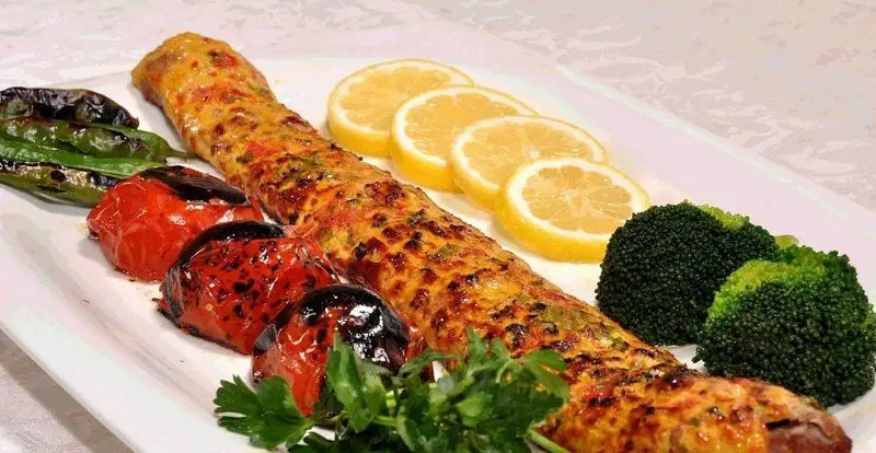 تصویری از یک کباب لوله‌ای مخصوص یا کوبیده مرغ گریل شده، با گوجه و فلفل کبابی، برش‌های لیمو و بروکلی از رستوران و کترینگ مانی.